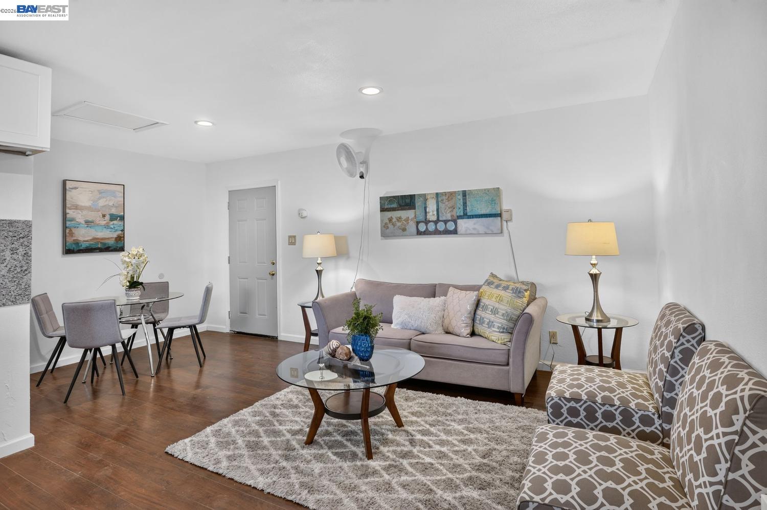 Living and dining area with a gray sofa, patterned armchairs, and a glass coffee table.