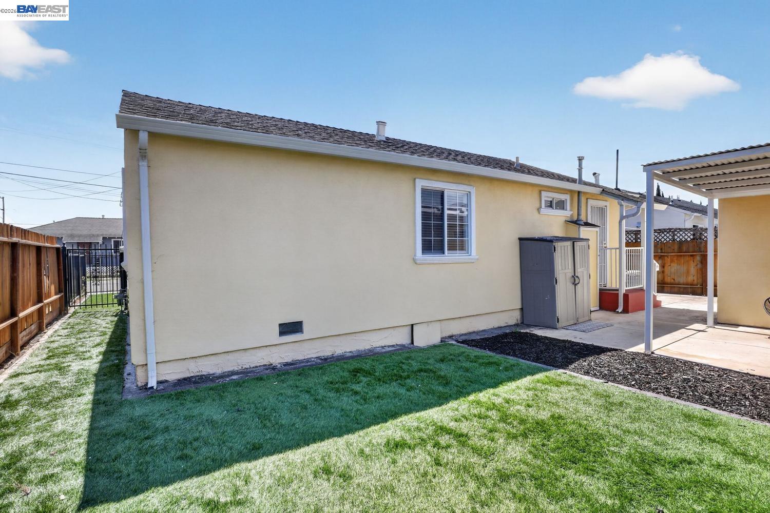 Rear of a pale yellow home with a covered patio and fenced grassy yard.