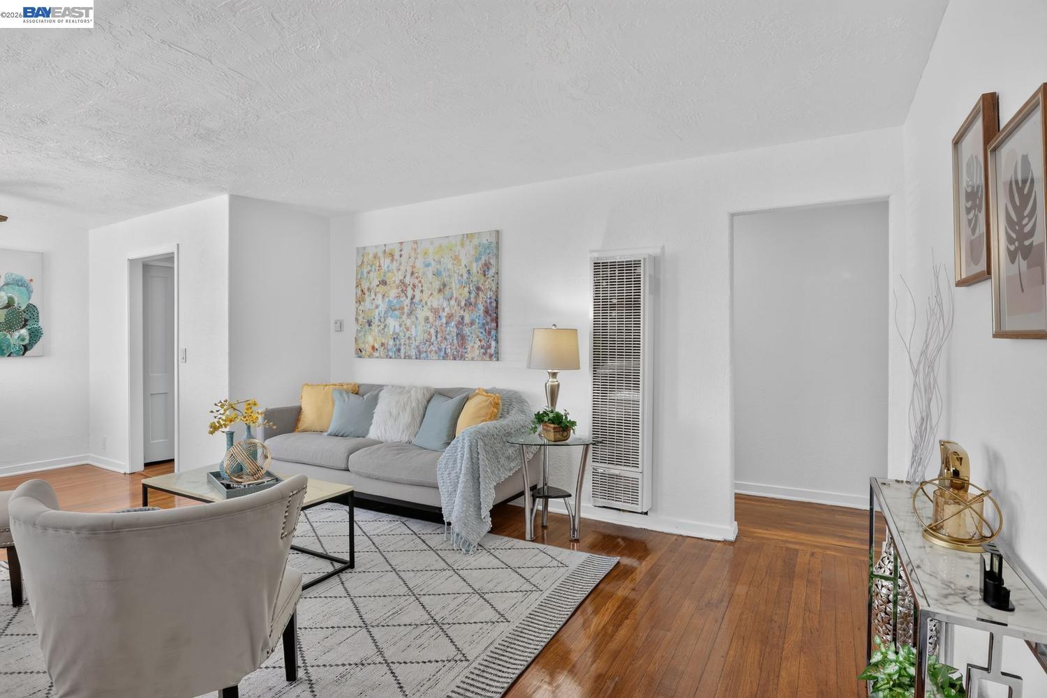 Furnished living room with a gray sofa, colorful abstract art, geometric rug, and warm hardwood floors.