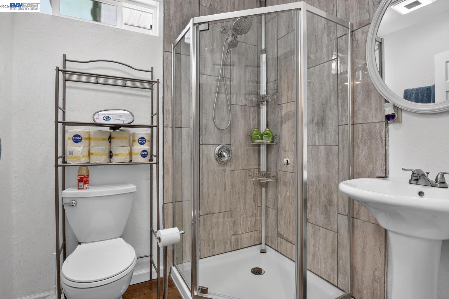 Bathroom with a glass-enclosed gray-tiled shower, white toilet, and pedestal sink.