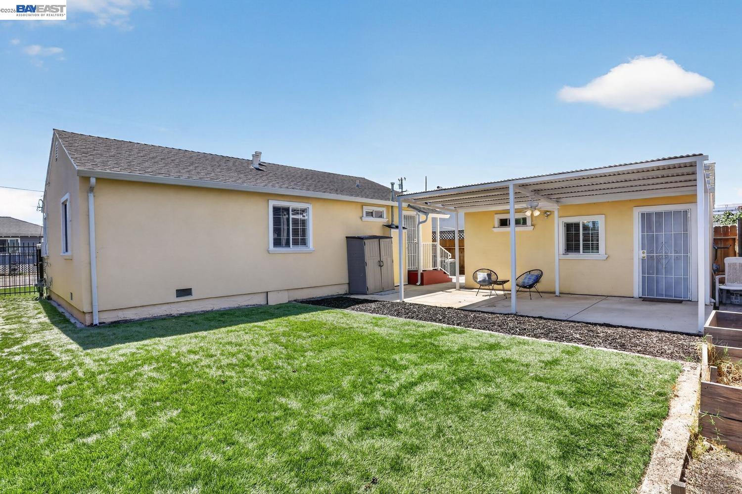 Rear of a yellow house with a covered patio and broad green lawn.