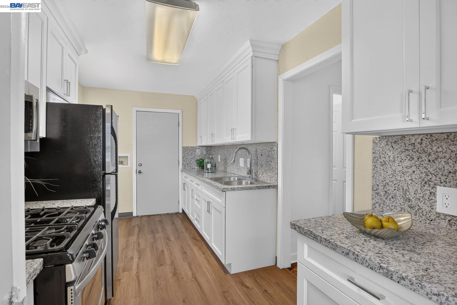 Kitchen with white cabinets, granite counters, stainless steel range, black refrigerator, and wood-look flooring.