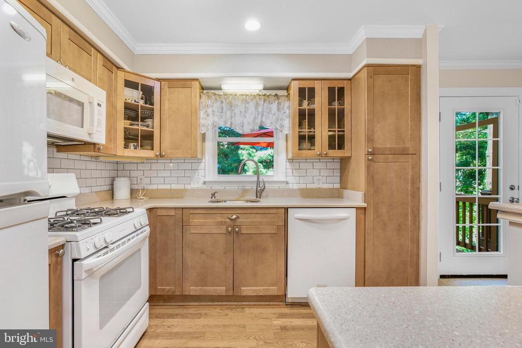 Kitchen with honey-colored cabinets, white subway tile, and a window overlooking greenery.