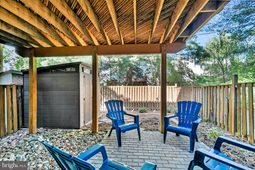 Covered backyard patio with blue Adirondack chairs, exposed timber beams, and a fenced yard.