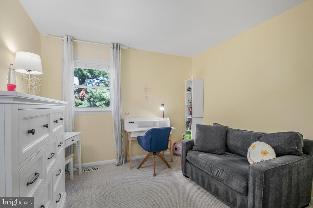Bedroom with gray sofa, white dresser, and desk beside a curtained window.