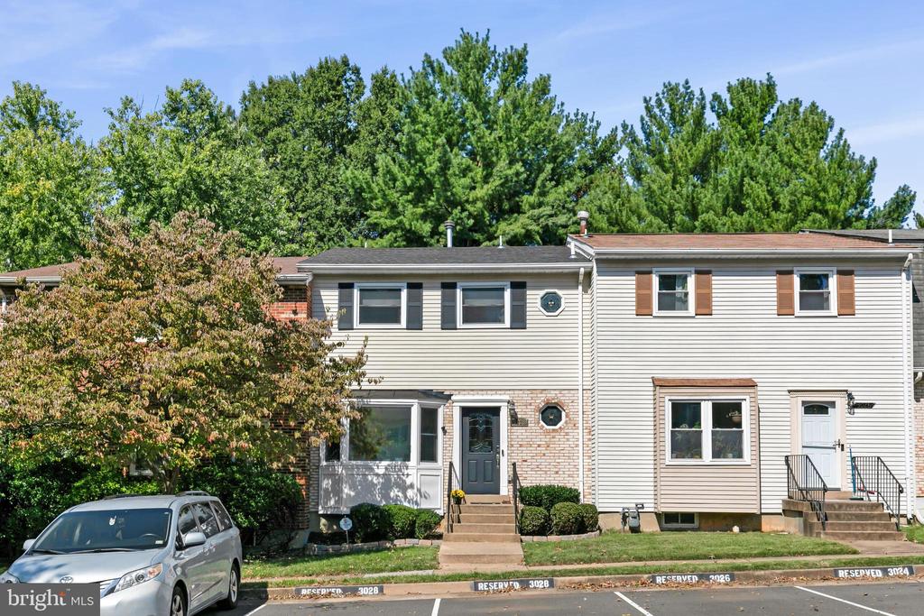 Two-story townhouse with light siding, brick accents, and a silver minivan parked in front.