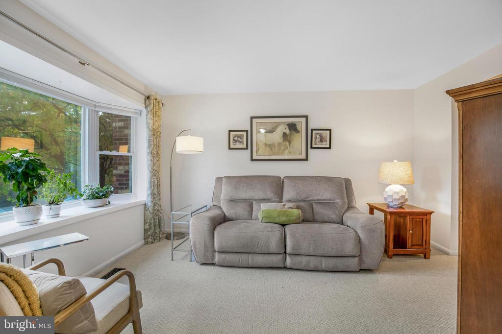 Living room with a gray reclining sofa, horse artwork, and a wide window overlooking greenery.