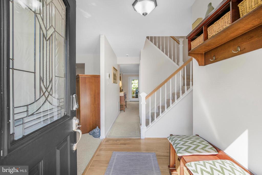 Entry foyer with a glass-paneled front door, hardwood floor, staircase, and wooden coat rack.