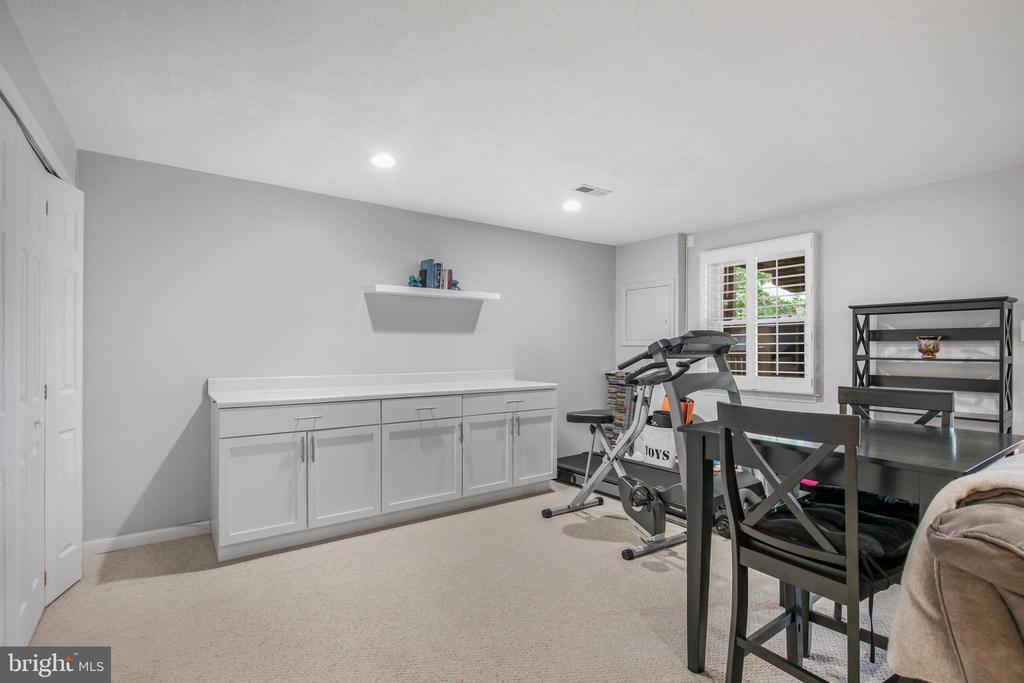 Finished basement recreation room with exercise equipment, dining table, and white built-in cabinets.
