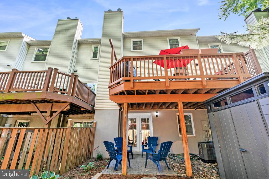 Home’s rear patio with elevated wooden decks, a red umbrella, and blue Adirondack chairs.