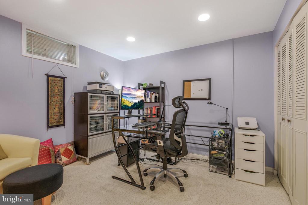Home office with lavender walls, a glass desk, ergonomic chair, and built-in storage cabinets.