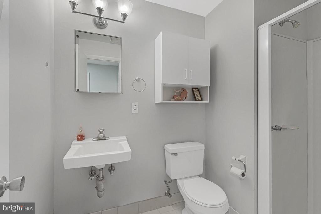 Bathroom with a wall-mounted sink, toilet, mirrored cabinet, and shower stall.