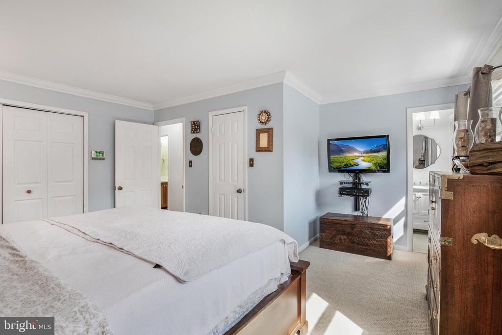 Bedroom with a white-covered bed, pale blue walls, and a wall-mounted television.