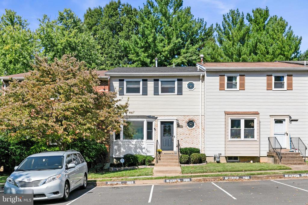 Townhouse exterior with light siding, brick accents, front steps, and reserved parking.