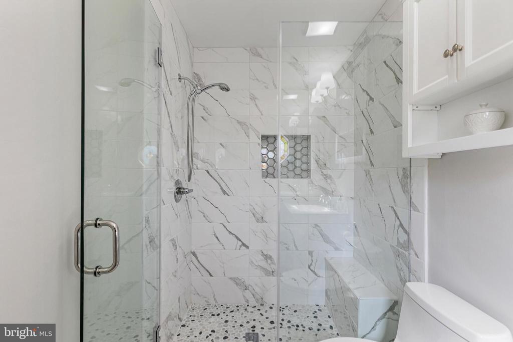 Bathroom with a glass-enclosed marble-look shower, pebble floor, and built-in tiled bench.