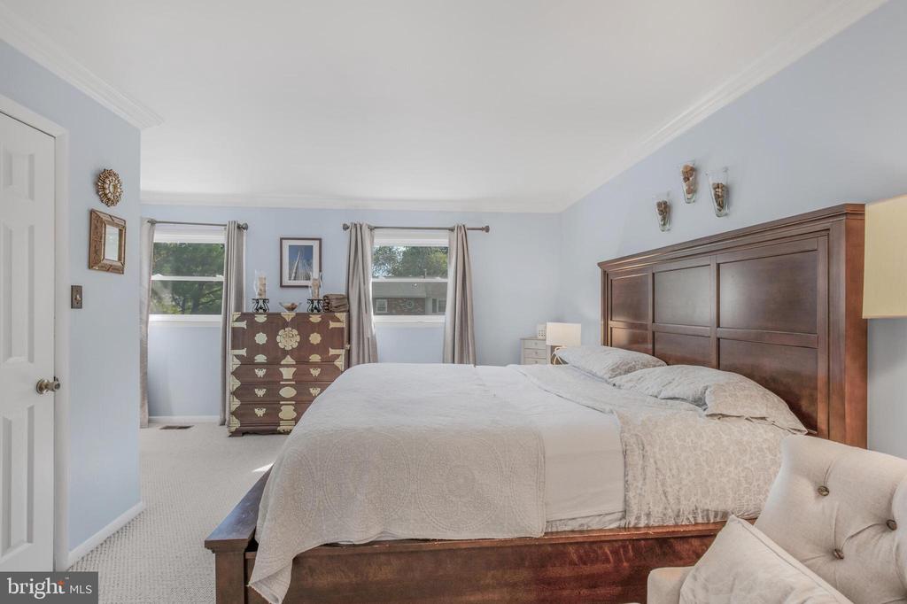 Bedroom with a dark wood bed, patterned white bedding, pale blue walls, and two windows.