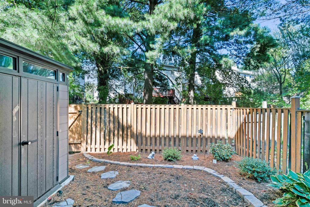 Backyard with a wooden privacy fence, gray shed, stone path, and mature trees.