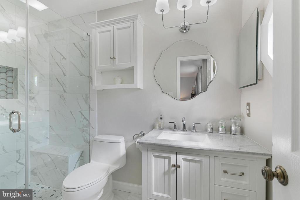 Bathroom with a marble-look walk-in shower, white vanity, and scalloped oval mirror.