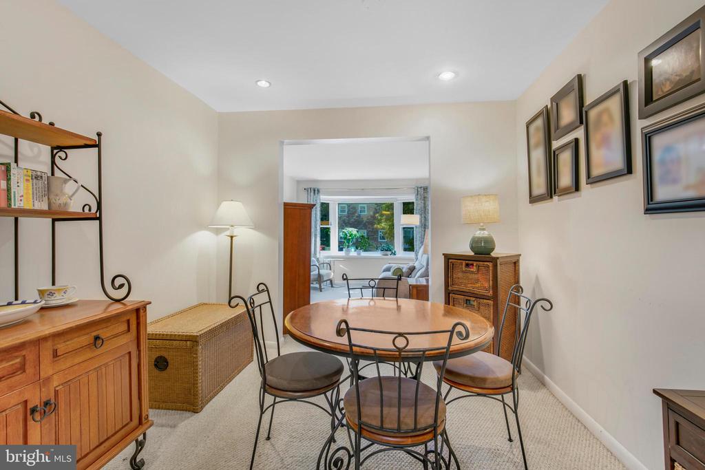Furnished dining room with a round wood table, black metal chairs, and a wide opening to a bright sitting room.
