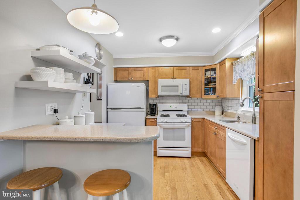 Kitchen with honey-colored cabinets, white appliances, and a breakfast peninsula with two stools.