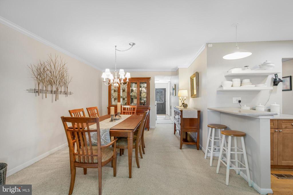 Dining room with a wooden table and chandelier beside an adjoining kitchen breakfast bar.