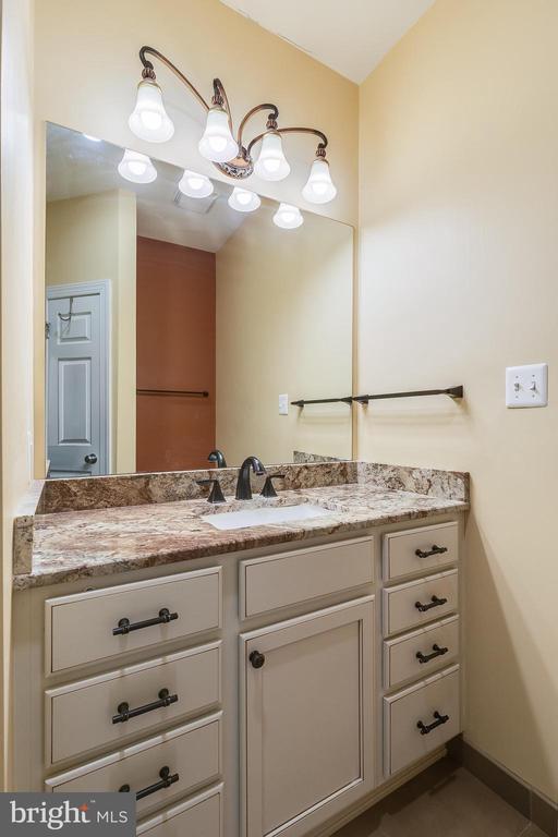Bathroom vanity with speckled granite countertop, dark faucet, and wide mirror beneath a multi-light fixture.