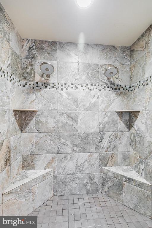 Walk-in shower with dual showerheads, built-in benches, and a mosaic accent band.