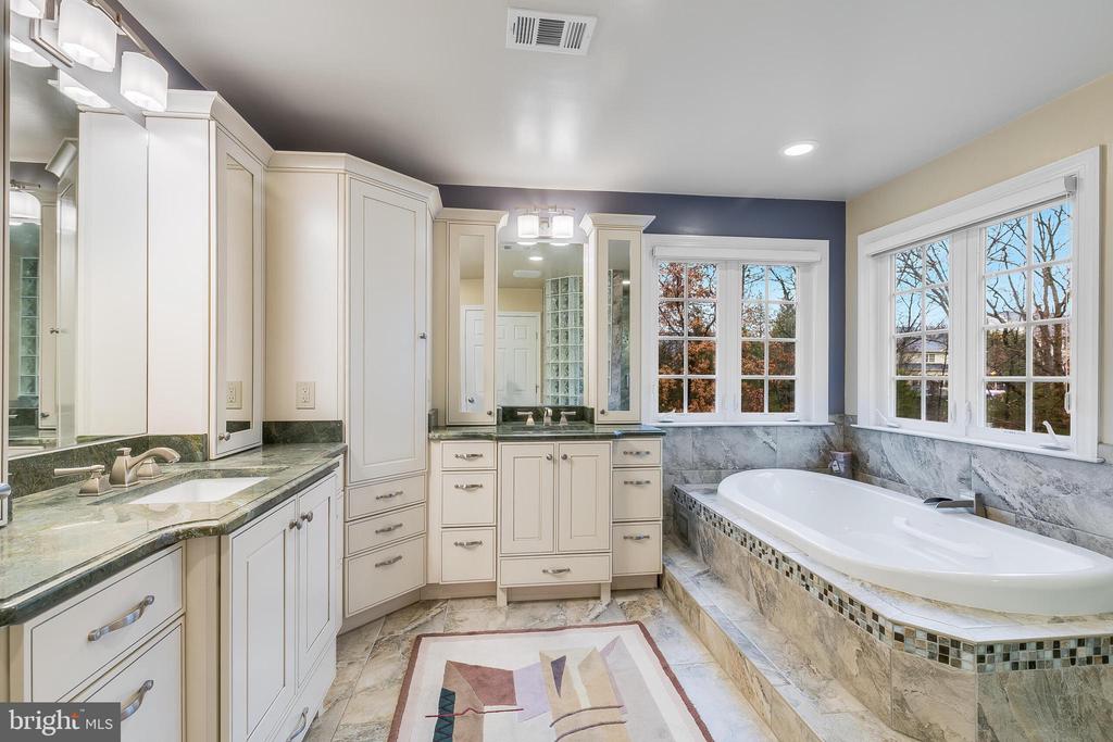 Spacious bathroom with cream cabinetry, marble finishes, a double vanity, and a soaking tub beneath large windows.