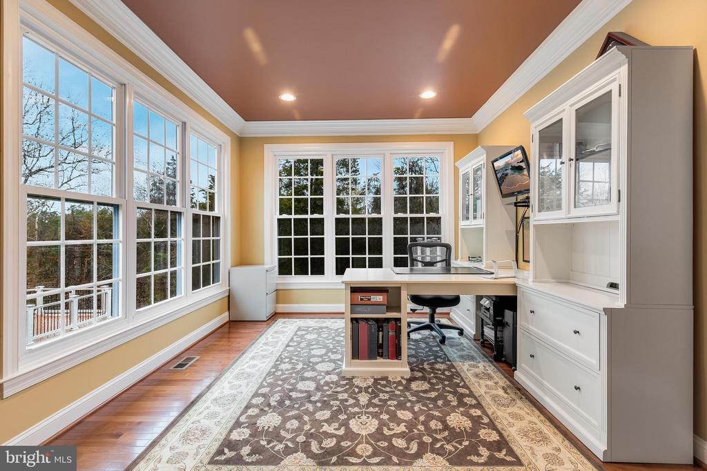 Home office with built-in cabinetry, a desk, and large windows overlooking trees.