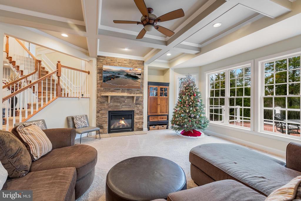 Living room with a stone fireplace, coffered ceiling, staircase, and decorated Christmas tree.
