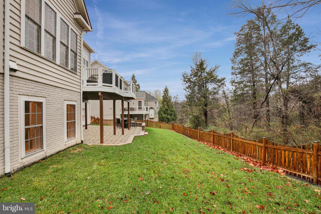 House rear exterior with raised deck, stone patio, and fenced grassy backyard.