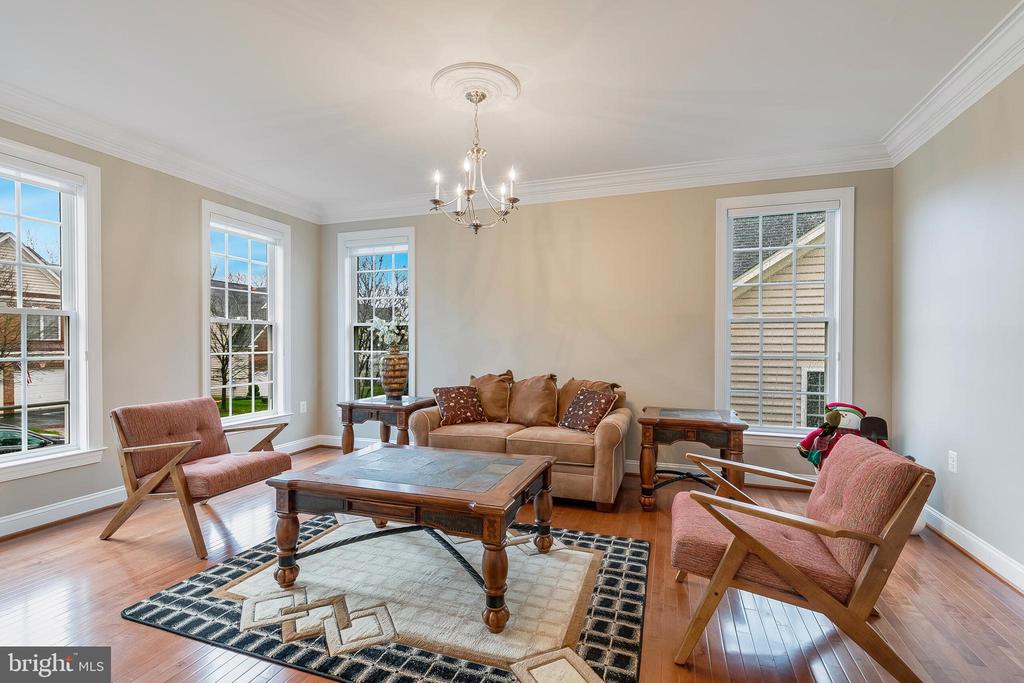 Living room with a tan leather sofa, pink armchairs, hardwood floors, and tall windows.