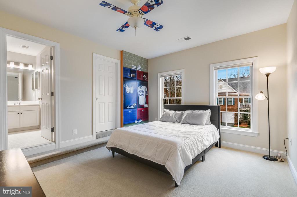 Bedroom with a white bed, sports-themed built-in display, and windows overlooking neighboring homes.