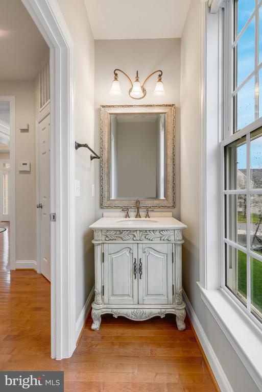 Powder room with an ornate pale gray vanity, framed mirror, and tall window.