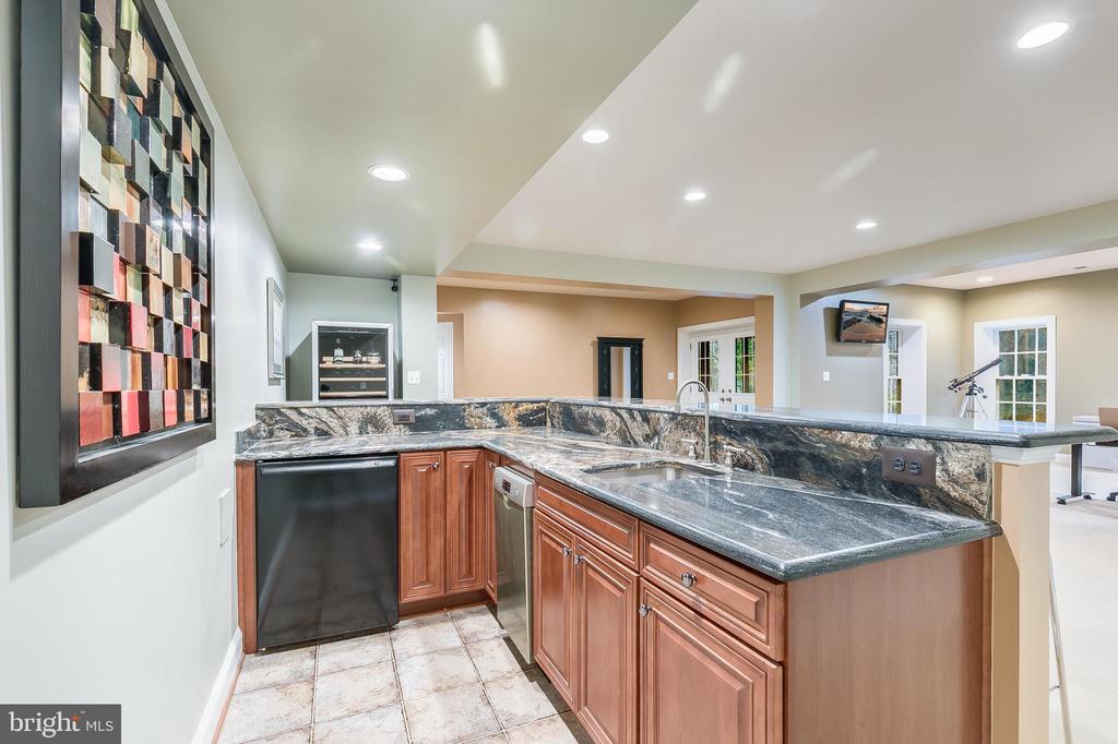 Basement wet bar with dark stone counters, warm wood cabinets, and an undercounter refrigerator.