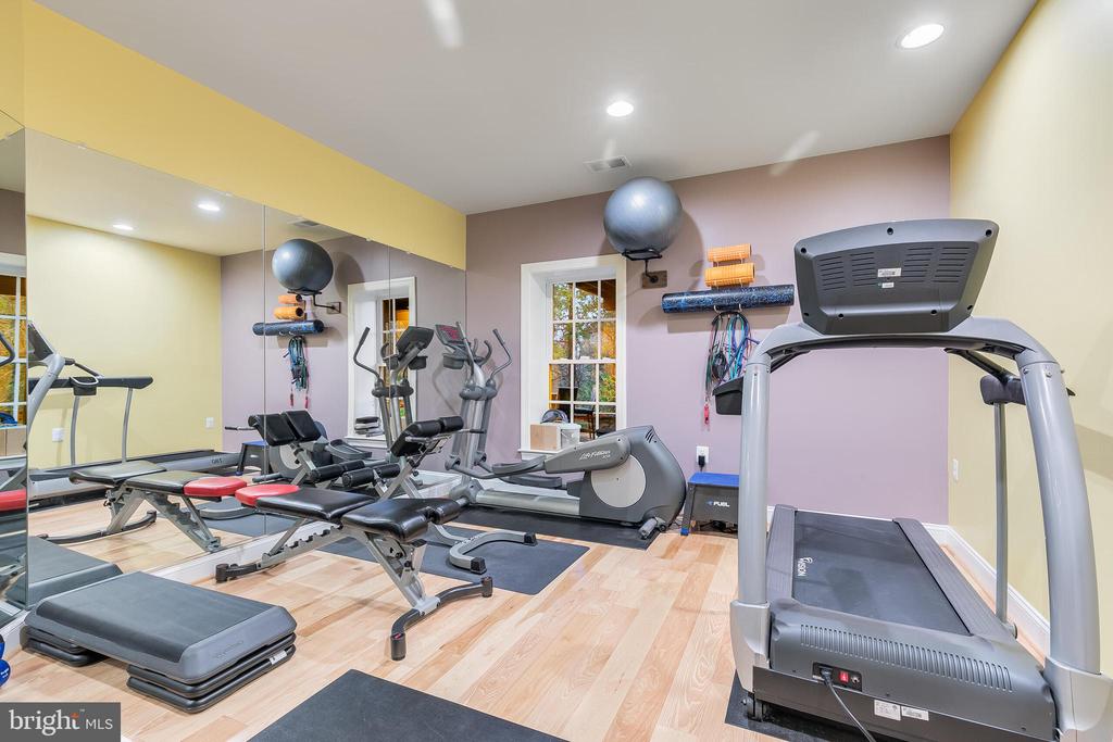 Home gym with a treadmill, stationary bike, weight bench, and mirrored wall.