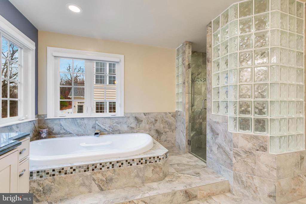 Bathroom with a large soaking tub, marble-look tile, and a glass-block shower partition.