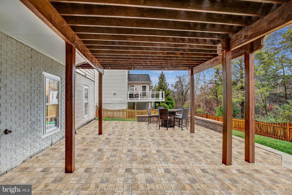 Covered patio with exposed wooden beams, tiled pavers, and an outdoor dining set.