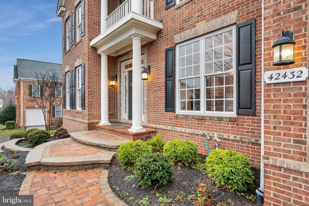 Brick home entrance with white columns, black shutters, brick walkway, and house number 42432.