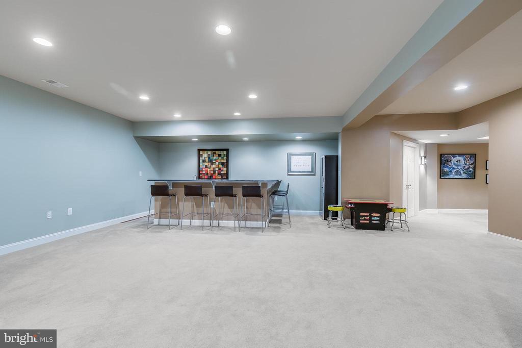 Finished basement recreation room with a bar counter, stools, and game table.