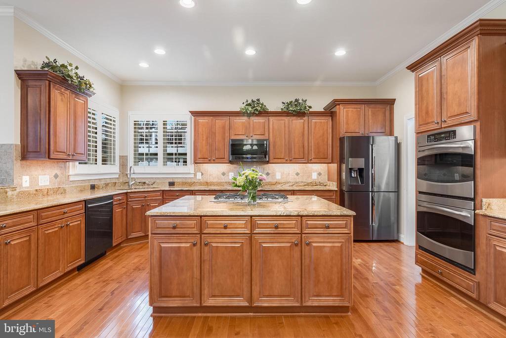 Kitchen with warm wood cabinetry, granite island, gas cooktop, and stainless steel appliances.