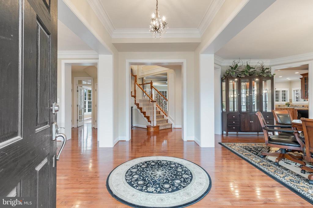 Foyer with polished hardwood floors, round rug, chandelier, and staircase.