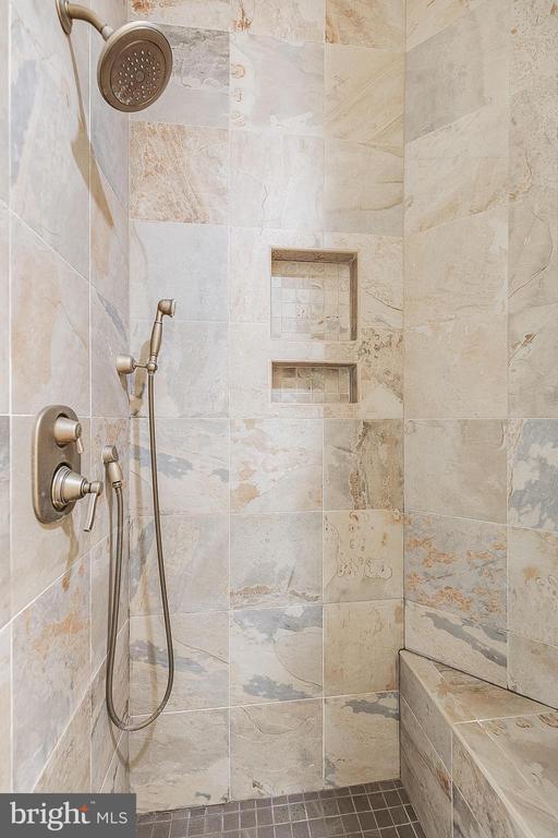 Walk-in shower with pale stone tile, a built-in bench, and bronze fixtures.