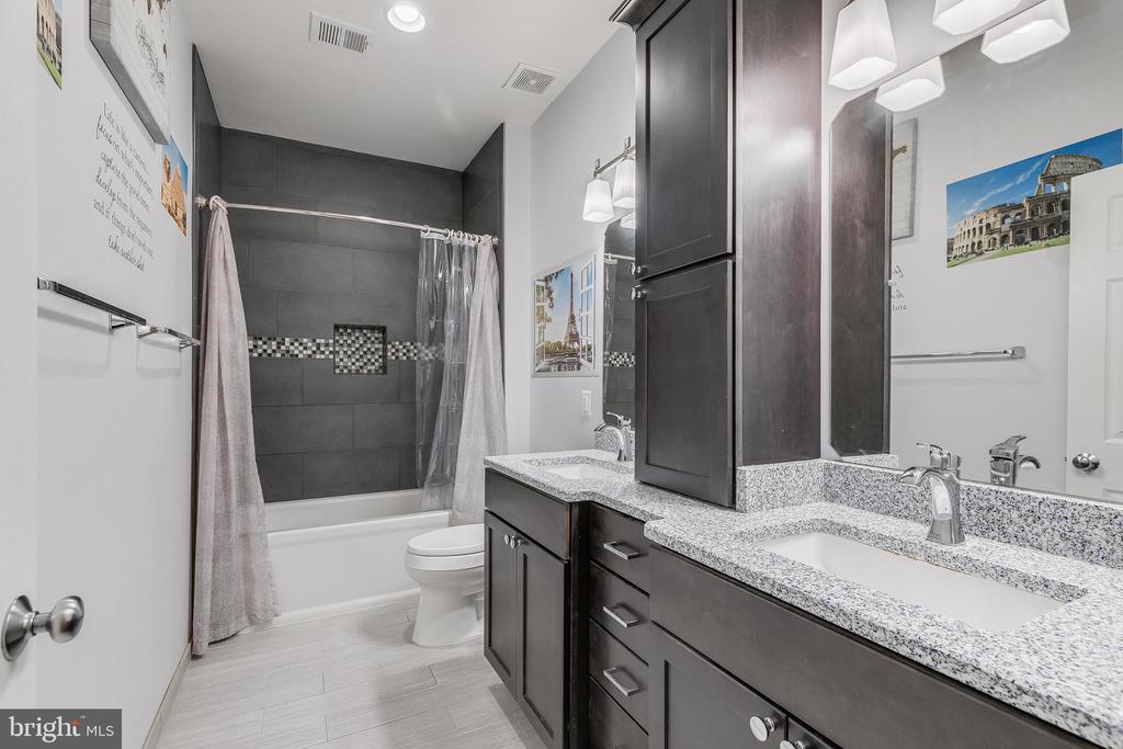 Bathroom with dark cabinetry, granite vanity, tiled tub-shower, and toilet.