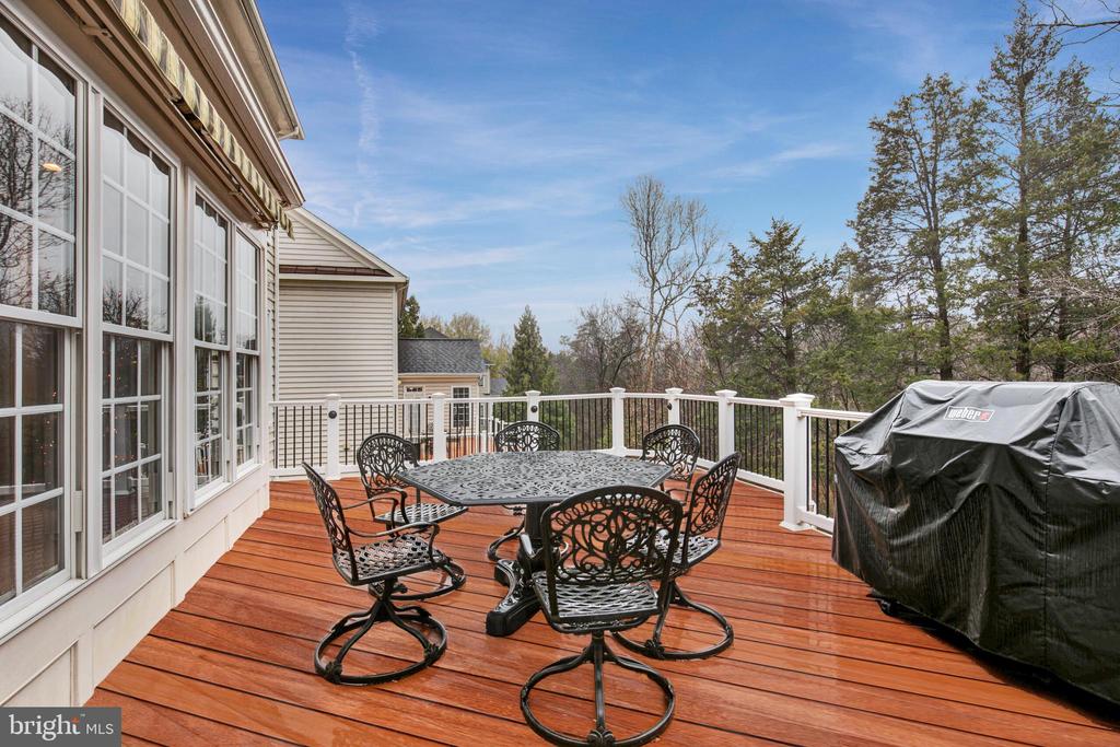 Deck with black metal dining set, white railings, and a covered grill overlooking trees.