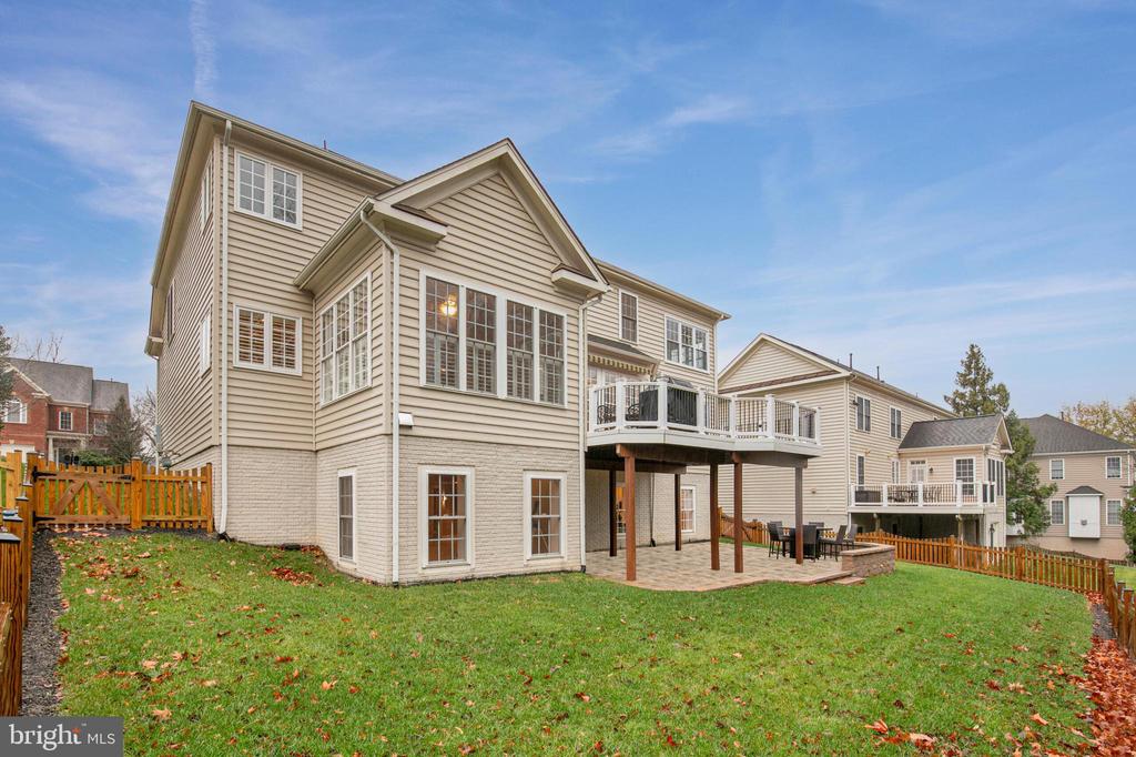 Rear exterior of a beige two-story home with an elevated deck, patio, and broad lawn.