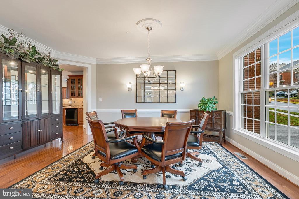 Dining room with a wooden table, leather chairs, ornate rug, and tall street-facing windows.
