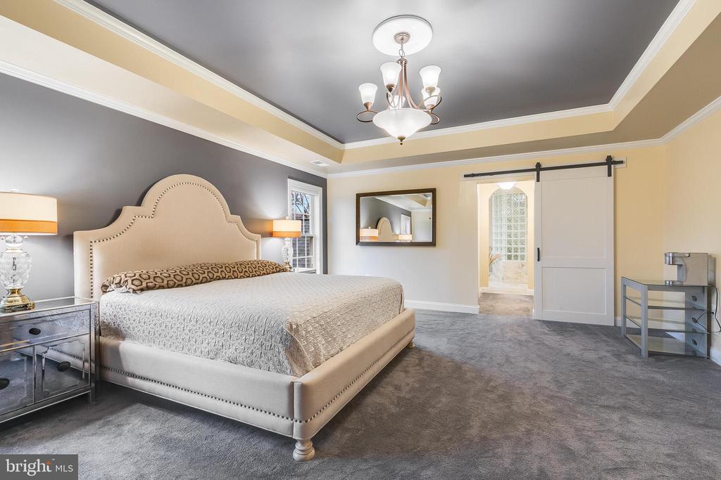 Furnished bedroom with an upholstered bed, tray ceiling, chandelier, and sliding barn door.