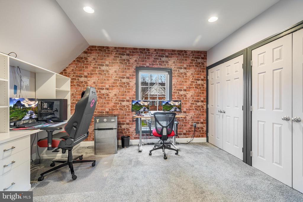 Home office with a brick accent wall, dual computer workstations, gaming chairs, and built-in cabinetry.