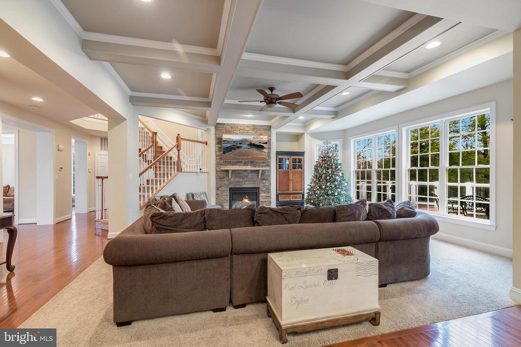 Living room with a stone fireplace, coffered ceiling, staircase, and decorated Christmas tree.